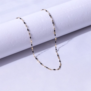 Detailed shot of a gold lip chain necklace featuring black oval beads on a purple fabric