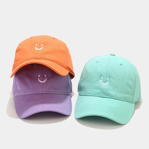 Detail of orange, purple, and mint green cotton baseball caps with smiley face embroidery