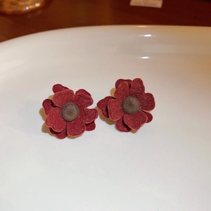 Detail of red floral velvet earrings with gold-plated pins on a white ceramic plate