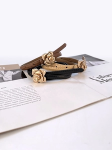 Three slim leather belts with gold rose buckles displayed on a fashion magazine