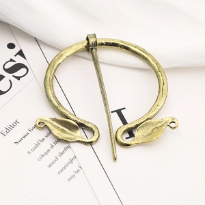 Detailed view of vintage Viking leaf brooch in gold metal on a fabric and book background