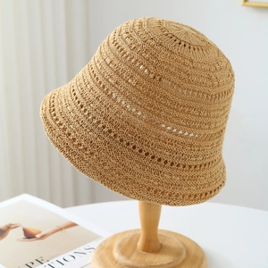 Handwoven khaki hollow straw bucket hat for women on a wooden stand in a bright room