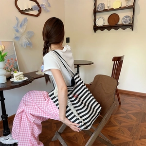 Detail of a large black and white striped canvas tote bag with red embroidery in a cafe setting