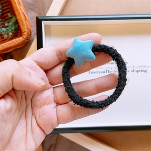 Dettaglio di un elastico per capelli nero in peluche con ciondolo a stella blu su legno