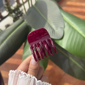 Glossy burgundy red hair claw clip held by hand with elegant lifestyle background