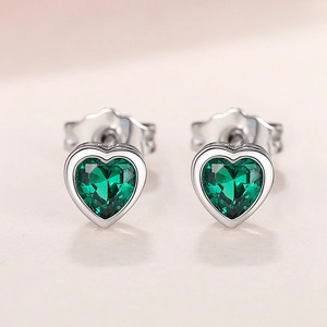 Macro detail of heart-cut green gemstone earrings with polished silver metal and butterfly backs