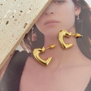 Detail of glossy gold heart-shaped stud earrings on a beige travertine stone background
