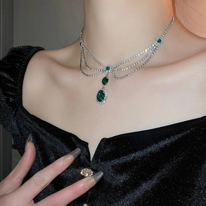 Detailed view of layered silver necklace with vibrant emerald green zircon pendants