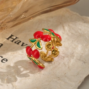 Artistic shot of a gold cherry open ring with red and green enamel on textured paper