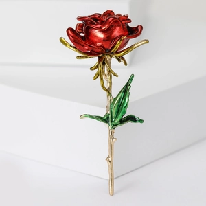 Macro detail of red rose brooch with golden stem and green enamel leaf design