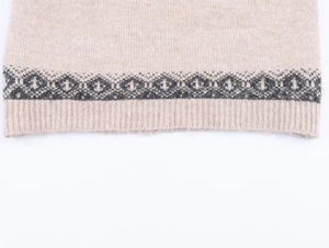 Close-up of beige knit sweater showing ethnic geometric jacquard and ribbed hem detail