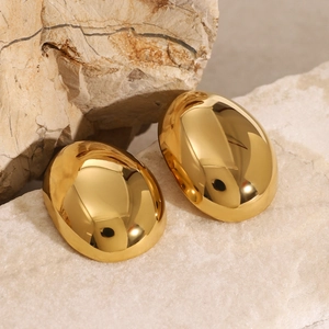 Macro detail of large oval gold earrings on natural stone showing high polish finish