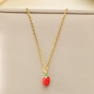 Dettaglio di una collana con ciondolo fragola rossa e catena dorata su tessuto beige