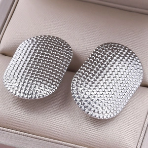 Macro detail of silver stainless steel earrings with textured honeycomb pattern surface