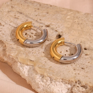 Detailed view of two-tone gold and silver C-shaped hoop earrings on stone surface