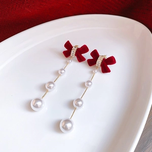 Detail of red velvet bow earrings with cascading white pearl tassels for a festive look