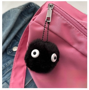 Gros plan du pendentif boule de suie en peluche noire sur un sac bandoulière rose en oxford
