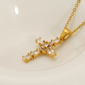 Golden cross pendant necklace with round and marquise-cut zircons in a white ceramic dish