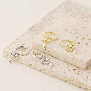 Macro shot of gold and silver bow-knot huggie earrings on a beige travertine stone