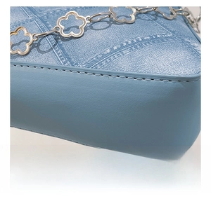 Detailed close-up of smooth stitching and silver floral chain on light blue denim bag