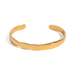 Close-up of golden stainless steel cuff bracelet with irregular wave texture