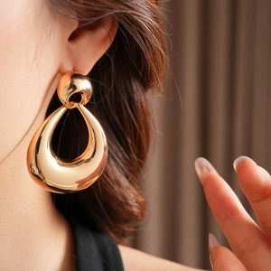 Close-up of model wearing large hollow teardrop golden metal earrings with stud detail