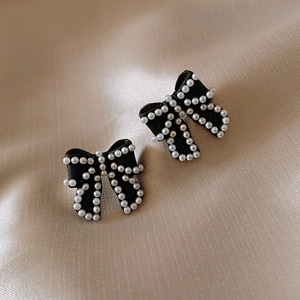 Macro shot of elegant black bow earrings with white pearls on champagne silk fabric