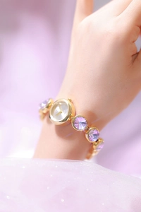 Gros plan sur une montre dorée pour femme ornée de cristaux violets sur le bracelet