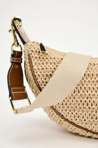 Detail of beige straw woven crossbody bag with brown leather trim and golden metal hardware