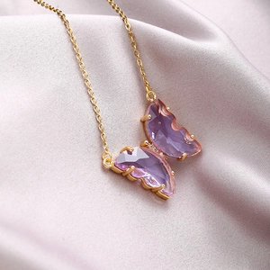 Detail of purple crystal butterfly pendant with gold chain on soft silk background