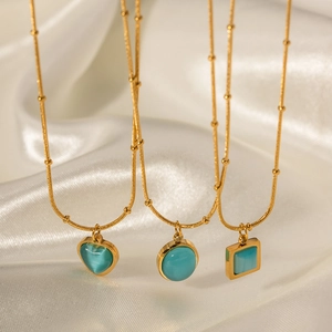 Detail of three gold necklaces with square, round, and heart-shaped turquoise cat-eye stones