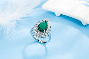 Close-up of pear-shaped emerald green gemstone ring with sparkling zircon halo setting