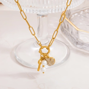 Detail of gold pearl necklace with heart pendant and key charm on glass stand