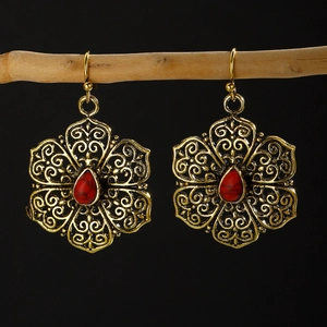 Detail of gold filigree earrings with red teardrop stone hanging on a wooden branch