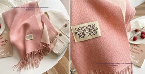 Detail of double-sided cashmere-like scarf in soft pink and beige with tassel trim