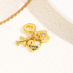 Detailed view of gold travel pendants featuring airplane, heart, and luggage on beige