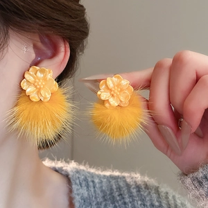 Close-up of stylish yellow flower stud earrings with soft plush pompom pendants