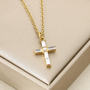 Close-up of gold-plated cross necklace with baguette zirconias and a center pearl