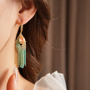Detail of bohemian gold tassel earring with turquoise beads and peach teardrop stone
