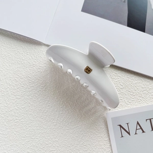 Detail of white acetate shark hair claw clip with gold B letter and magazine backdrop