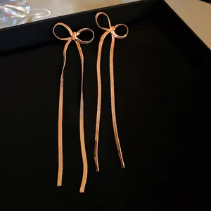 Vue macro de boucles d'oreilles nœud en or rose avec longues chaînes à pompons sur velours