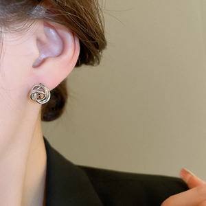Macro view of minimalist silver intertwined hoop earrings worn on a model ear