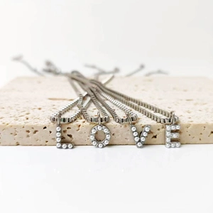 Detalle de colgantes de letras LOVE en acero plateado con perlas en cadenas de caja