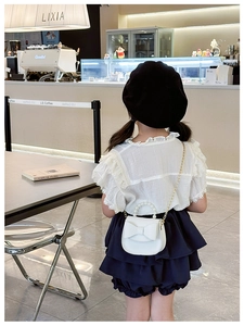 Detail showing white kids crossbody bag with pearl handle and bow in modern cafe setting