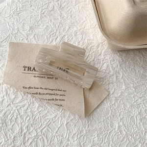 Macro detail of square acetate hair claw clip with cream marble pattern on canvas background