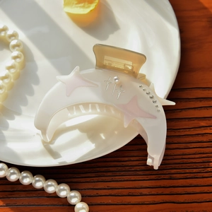 Detailed view of crescent moon hair claw clip with star rhinestones and pearls on a plate