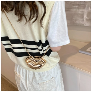 Détail d'un sac à main doré en forme de lèvres avec une fine bandoulière en chaîne