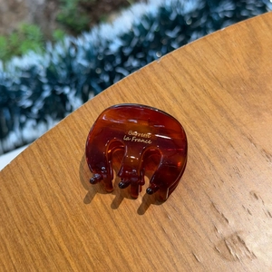 Amber acetate hair claw clip with golden M letter on rustic wooden surface
