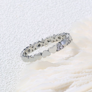 Macro detail of silver heart-shaped ring band with clear zircon accents on white coral