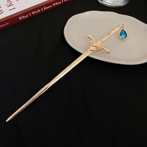 Detailed macro view of a gold sword hairpin with a blue teardrop gemstone pendant